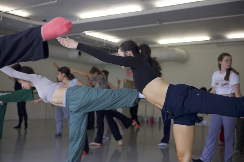 Dance students pose with extended arms and legs during a dance class in a rehearsal studio